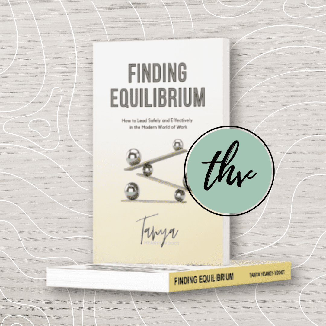 A book titled "Finding Equilibrium" by Tanya Heaney-Voogt is shown standing upright, with a cover featuring balanced spheres on seesaws.